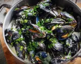En stor gryta med ångande moules marinières, toppad med färsk persilja och serverad i en krämig vitvinssås.