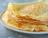 En hög med gyllene, tunna pannkakor på en vit tallrik. Perfekt för ett enkelt pankakor recept.