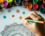Mano che colora con una matita un disegno di mandala. Piccoli cerchi colorati e vasetti di pittura sullo sfondo.