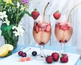 Två glas med drink med gin och prosecco, fyllda med is, jordgubbar och körsbär. Garnerade med jordgubbar och serverade med blommor och citron.