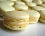 Un délicieux macaron meringue française, à la garniture crémeuse, se tient au premier plan, entouré d'autres macarons pâles.