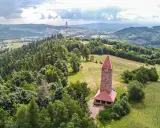 Kamienna wieża widokowa na wzgórzu, otoczona lasami i polami. Jedna z wielu wież widokowych na Dolnym Śląsku, oferująca malownicze krajobrazy.