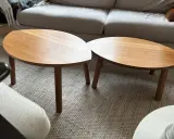 Två ovala soffbord i trä, liknande IKEA:s soffbord i Stockholm, står på en matta framför en soffa.