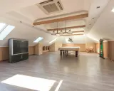 Vaste pièce sous les combles aménageables, avec table de billard, TV, fauteuil à bascule et étagères. Idéal pour un espace de loisirs.