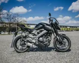 Czarny motocykl Yamaha MT-125, model kat a1, zaparkowany na żwirowym placu przed budynkiem.