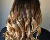 Piękne, falowane włosy z subtelnymi refleksami blond na ciemnych włosach, tworzące efekt ombre.