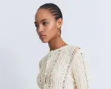 Mujer con trenzas luciendo un cárdigan de ganchillo blanco con intrincados patrones.