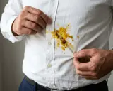 Mann zeigt gelbe Curryflecken auf weißem Hemd. Tipps zum Curryflecken entfernen gesucht.