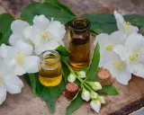 Deux petites fioles d'huile essentielle fleur d'oranger, entourées de fleurs de jasmin blanches et de feuilles vertes sur un fond de bois.