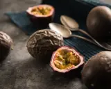 Reife Passionsfrüchte, eine aufgeschnitten, zeigen ihr saftiges Inneres. Zwei Löffel liegen bereit, um die exotische Frucht zu genießen.