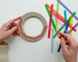 Hände bereiten einen Ring für Fenstersterne vor, indem sie bunte Streifen zum Falten bereitlegen.