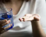 Une main tient un comprimé, peut-être un supplément de sels minéraux, à côté d'un verre d'eau bleue.