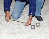 Un joueur de pétanque mesure la distance entre les boules. On se demande combien gagne un joueur de pétanque professionnel.