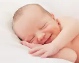 Un bebé duerme plácidamente, con una sonrisa que nos hace preguntar porque sonrien los bebes. Su carita refleja paz y felicidad.