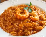 Delicioso arroz caldoso con gambas y trozos de calamar, adornado con una ramita de perejil.