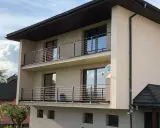 Nowoczesny dom z dwoma balkonami, gdzie zamiast tradycyjnej balustrady zastosowano elegancki murek z poziomymi stalowymi elementami.