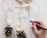 Déco Noël pomme de pin à faire soi-même : des suspensions naturelles avec perles en bois et messages personnalisés.