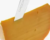 Ein Messer schneidet ein Stück leuchtend orangefarbenen Cheddar-Käse. Was ist Cheddar? Ein köstlicher Hartkäse.