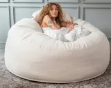 En kvinna med lockigt hår vilar i en stor, mjuk beige sittpall.