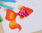 Bunter Fisch mit bunten Schuppen, inspiriert von der Frage: was soll ich malen kinder. Buntstifte liegen daneben.