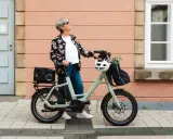 Ältere Dame mit QIO Bike, positive Erfahrungen mit dem E-Bike, das mit einem Helm und einer Tasche beladen ist.