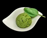 Une cuillère de pesto maison, d'un vert vibrant, garnie d'une feuille de basilic frais, dans une coupelle blanche.