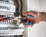 Elektryk pracuje przy skrzynce z bezpiecznikami. Gdy zgłosić brak prądu, warto sprawdzić właśnie takie instalacje.