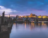 Nastrojowa fotografia nocna Pragi: Most Karola i Zamek na Hradczanach w blasku świateł, odbijających się w Wełtawie.