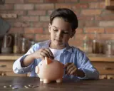 Niño introduce una moneda en una hucha rosa, aprendiendo sobre el ahorro con la cuenta infantil BBVA.
