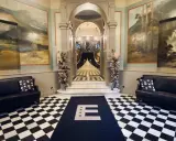 Elegant foajé med schackrutigt golv, konstverk på väggarna och en trappa. En matta med bokstaven E leder mot trappan. Känns som en plats med mycket hotell Knaust historia.