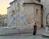 Sculture di due uomini che si spingono a San Quirico d'Orcia, con una donna con ombrellino.