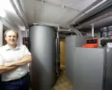Mann vor Pelletheizung und großem Speicher in Heizungsraum.