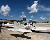 Zwei ultraleichtflugzeug modelle stehen auf dem Rollfeld. Im Hintergrund ein Kontrollturm und weitere Flugzeuge.