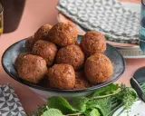 Un piatto colmo di polpette di fagioli dorate, guarnito con erbe fresche.