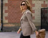 Elegancka kobieta po 50. w beżowej marynarce i okularach przeciwsłonecznych, niosąca brązową torbę. Stylowa moda dla pań po 50.