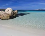 Spiaggia bianca e rocce granitiche sull'isola della Maddalena, con acque cristalline e un cielo azzurro intenso.