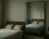Un grand miroir en face du lit reflète la chambre, créant une impression d'espace et de sérénité. La lumière douce filtre à travers les rideaux.