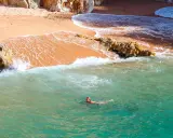 Eine Frau schwimmt im türkisfarbenen Meer vor einer sandigen Bucht in Palamós, Spanien.