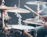 Gros plan sur un set de batterie, avec des baguettes en action. Différents types de tambour et cymbales sont visibles.