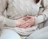 Kobieta trzyma się za brzuch, odczuwając ból brzucha po jedzeniu.
