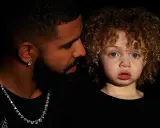Drake i jego syn, Adonis, w czarnych ubraniach. Chłopiec ma kręcone, jasne włosy i niebieskie oczy.