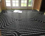 Instalación suelo radiante con tuberías blancas sobre paneles negros. Un plano yace sobre el suelo.