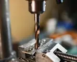 Wiertło wkręca się w metalowy element przytrzymywany przez imadło.