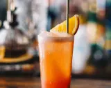 Orzeźwiający drink Garibaldi z plasterkiem pomarańczy i złotą słomką, idealny na letnie popołudnie.