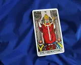 Karta Tarota "The Hierophant" na niebieskim tle. Postać w czerwonych szatach z tiarą i krzyżem.