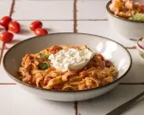 Pyszny makaron z kremową burratą i sosem pomidorowym, udekorowany natką pietruszki. Obok miseczka z rzodkiewką i pomidorki koktajlowe.