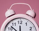 Różowy budzik z dzwonkami. Wskazówki pokazują godzinę 12:21. To znaczenie czasu, który ucieka.