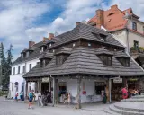 Urokliwy rynek w Kazimierzu Dolnym z charakterystycznymi kamieniczkami i drewnianymi dachami. Ludzie spacerują, kupują lody i pamiątki.