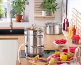 Saft einkochen im Einkochautomat: Obst wird im Dampfgarer zu Saft verarbeitet. Daneben stehen Gläser mit roter Johannisbeermarmelade und Flaschen mit Sirup.