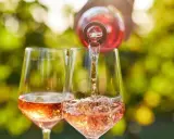 Le danger du vin rosé : une bouteille verse son contenu dans deux verres, créant une cascade pétillante sous un soleil radieux.